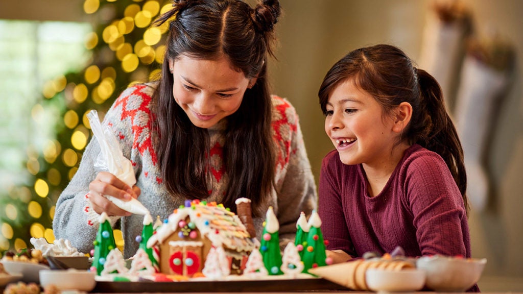 Girls decorating a gingerbread house.